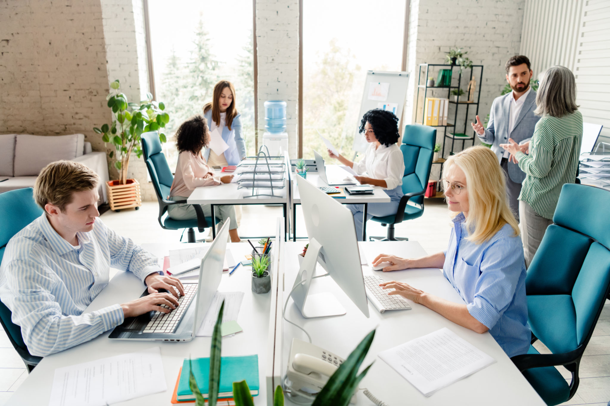 A busy office filled with professionals collaborating, working, and discussing projects, emphasizing teamwork and productivity in a stylish and well-lit environment.